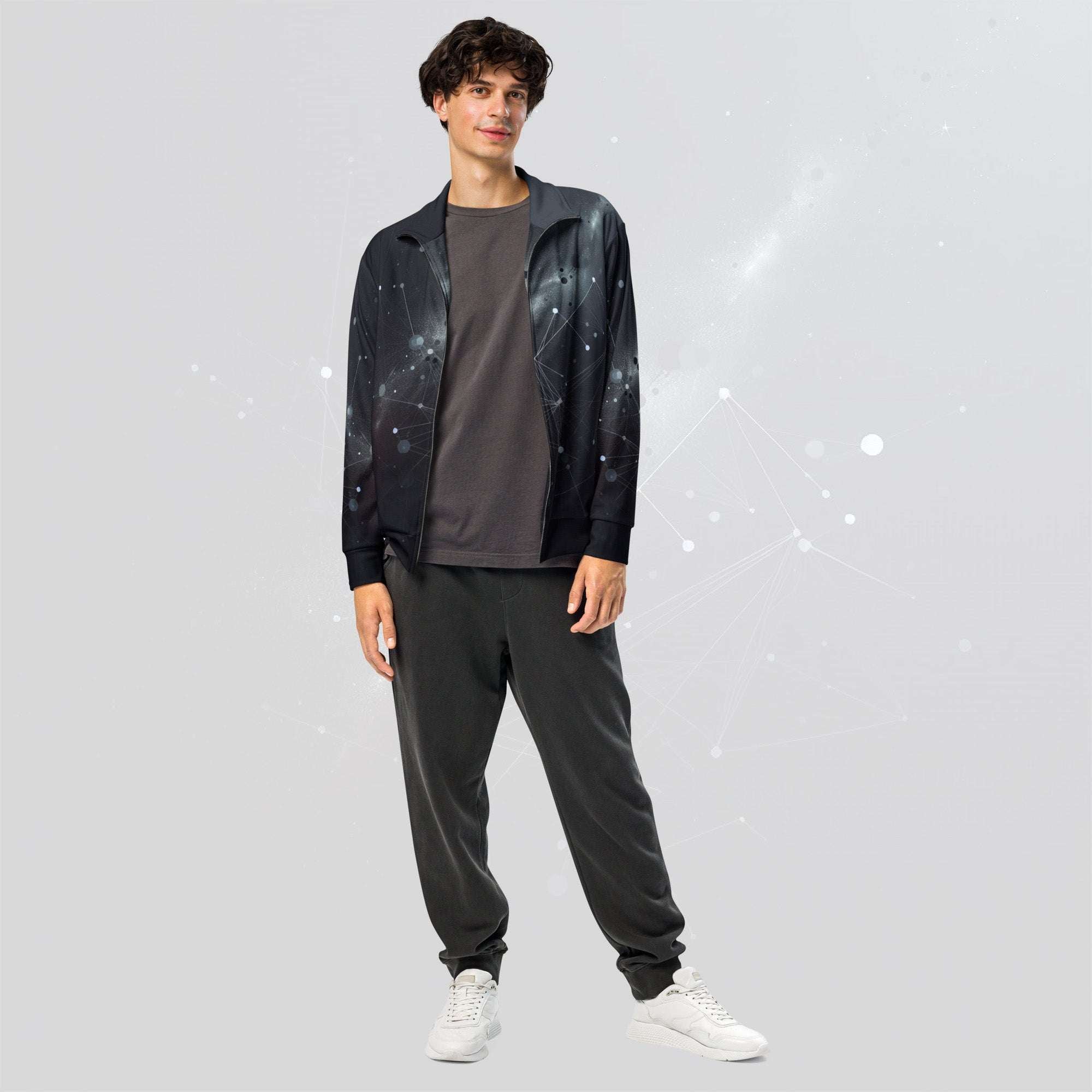 Male model wearing Men’s Constellation Stem Print (No.03) zip track jacket by Form Finding Design, front view worn open over a dark tee—constellation-web graphic across chest and sleeves, paired with dark joggers and white trainers.