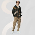 Male model wearing the Form Finding Design men’s Shadow Drip Hoodie (No.12) with the zip partly undone over a light‑coloured tee; the black hoodie’s earth‑toned abstract shapes stand out against khaki cargo trousers, as he poses with hands in his pockets on a pale grey background with faint arc motifs.