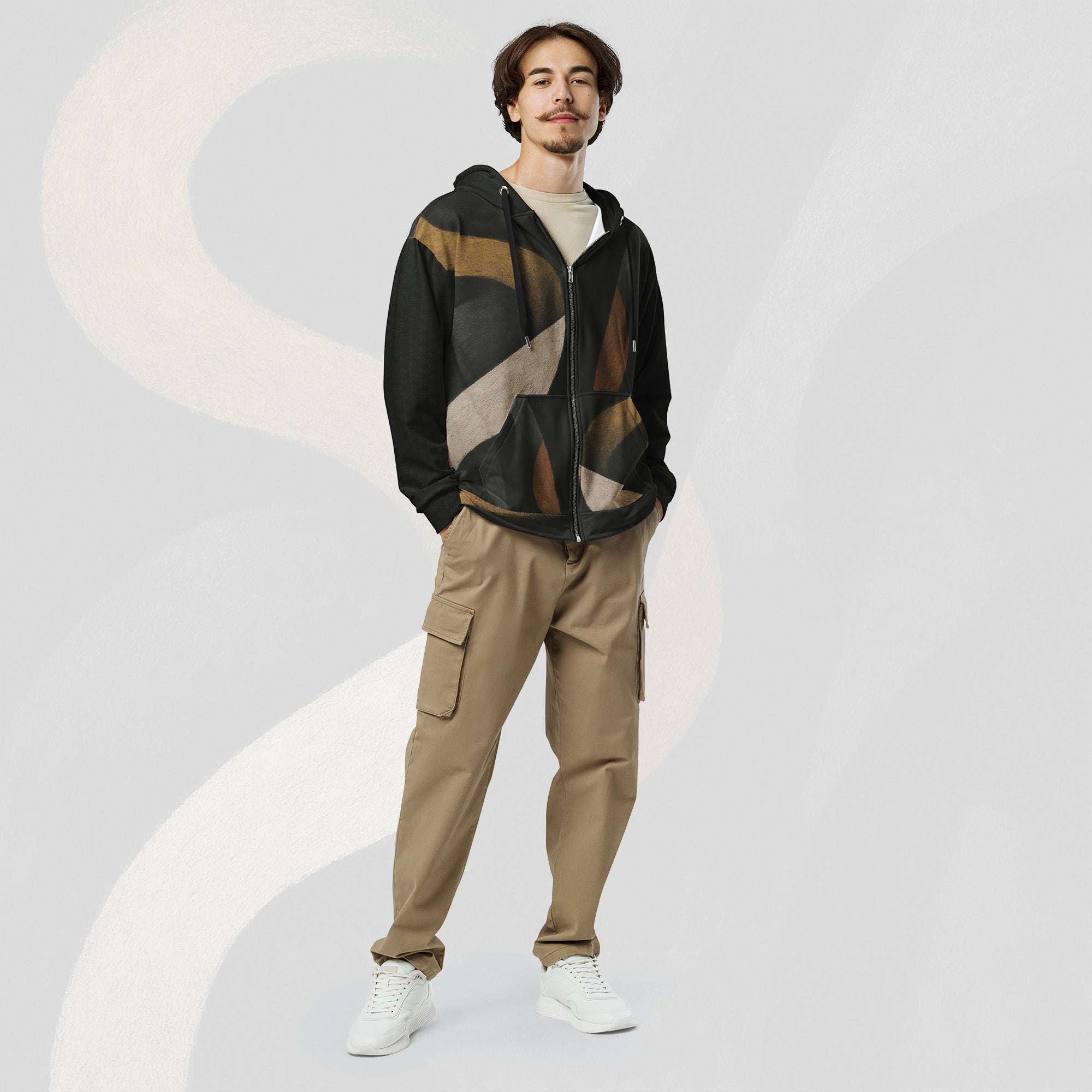 Male model wearing the Form Finding Design men’s Shadow Drip Hoodie (No.12) with the zip partly undone over a light‑coloured tee; the black hoodie’s earth‑toned abstract shapes stand out against khaki cargo trousers, as he poses with hands in his pockets on a pale grey background with faint arc motifs.