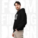 Three-quarter side portrait of male model in FormFD Men’s Signature Hoodie (FFD-08), black—hood drape, kangaroo pocket and partial chest logo visible, hand in pocket, beige chinos.