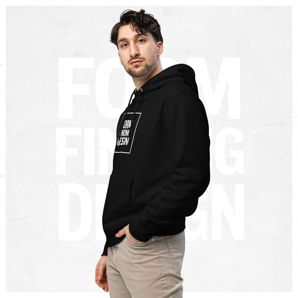 Three-quarter side portrait of male model in FormFD Men’s Signature Hoodie (FFD-18), black—hood drape, kangaroo pocket and partial chest logo visible, hand in pocket, beige chinos.