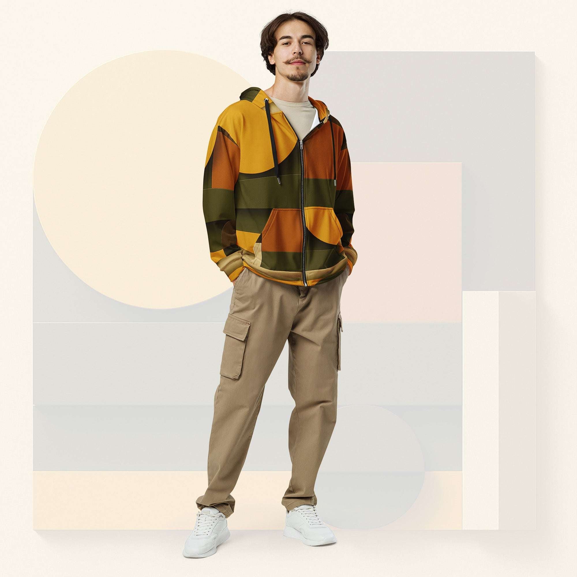 Male model wearing Form Finding Design Men’s Urban Utility Hoodie (No.09), front full-body—earth-tone geometric print zip hoodie with black drawstrings, styled with tan cargo trousers and white trainers, minimal architectural studio backdrop.