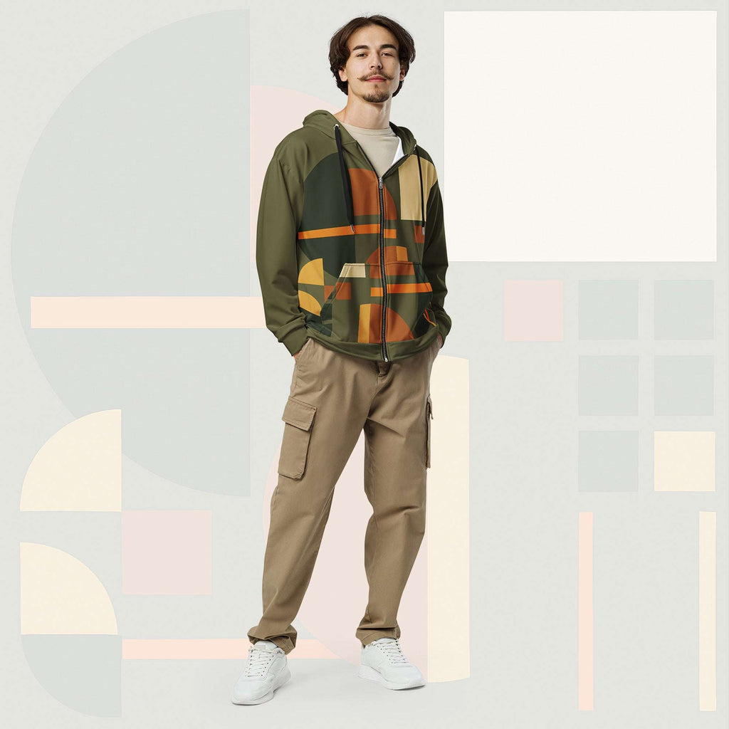 Male model wearing Form Finding Design Men’s Urban Utility Hoodie (No.12), front full-body—earth-tone geometric print zip hoodie with black drawstrings, styled with tan cargo trousers and white trainers, minimal architectural studio backdrop.