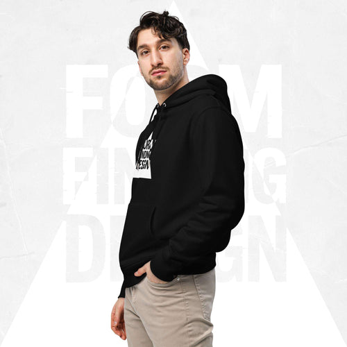 Three-quarter side portrait of male model in FormFD Men’s Signature Hoodie (FFD-12), black—hood drape, kangaroo pocket and partial chest logo visible, hand in pocket, beige chinos.