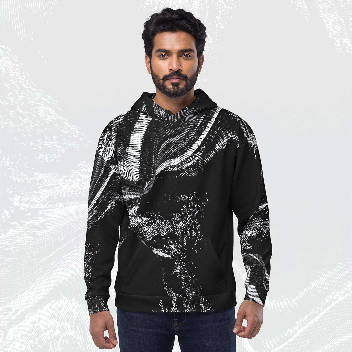 A man wearing a black pullover hoodie with a white abstract brushstroke pattern, paired with dark blue jeans, standing against a light gray textured background.