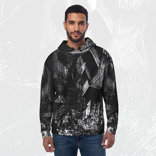A man wearing a black and white abstract patterned hoodie with blue jeans, standing against a light gray textured background.