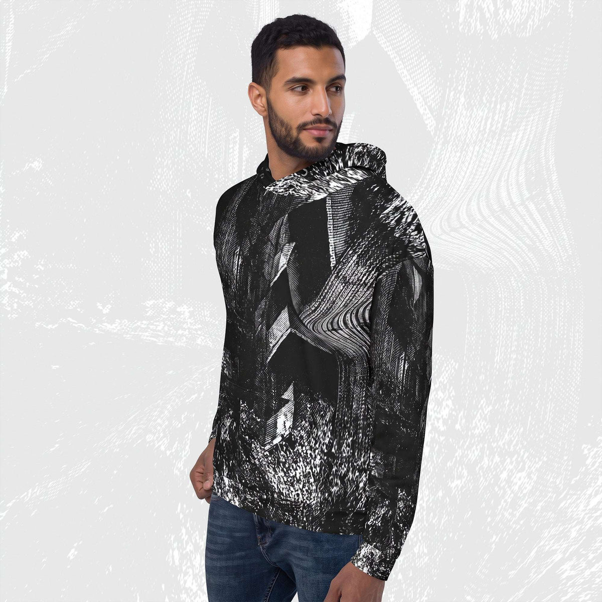 A man wearing a black and white abstract patterned hoodie with blue jeans, standing against a light gray textured background.