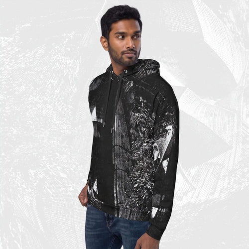 A man wearing a black pullover hoodie with a detailed black and white graphic print on the front and sleeves, paired with blue jeans, set against a light gray patterned background.