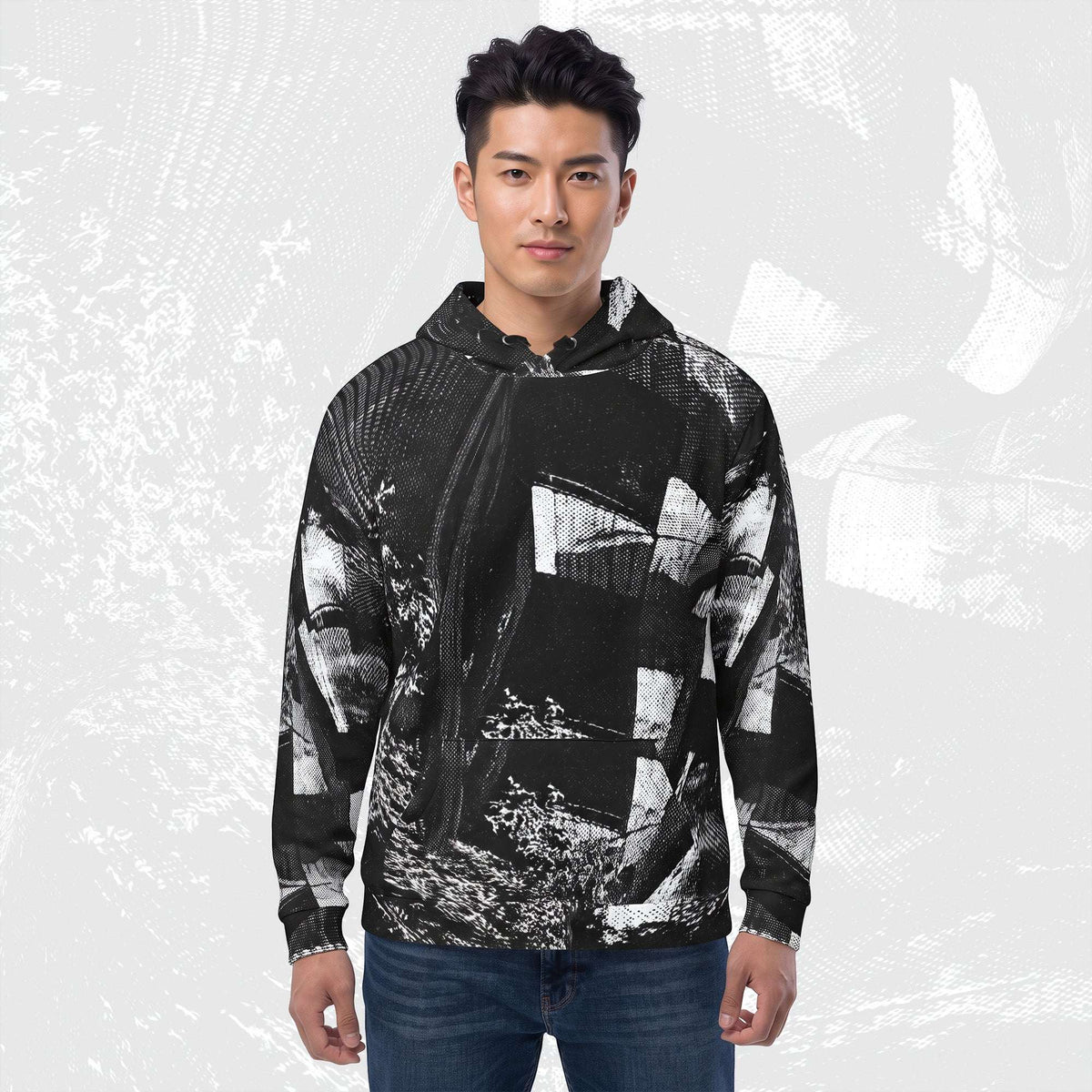 A man wearing a black and white abstract patterned zip-up hoodie with blue jeans, standing against a light gray textured background.