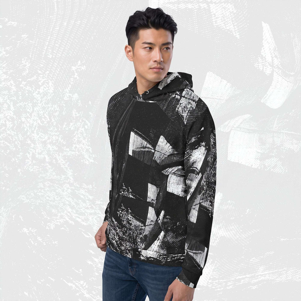 A man wearing a black and white abstract patterned zip-up hoodie with a drawstring hood, paired with blue jeans, standing against a light gray textured background.