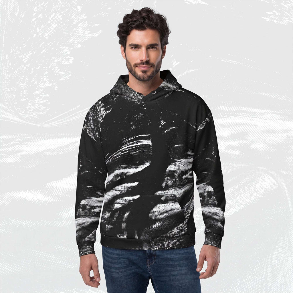 A man wearing a black pullover hoodie with a white and gray abstract brushstroke pattern, paired with blue jeans, set against a light gray textured background.
