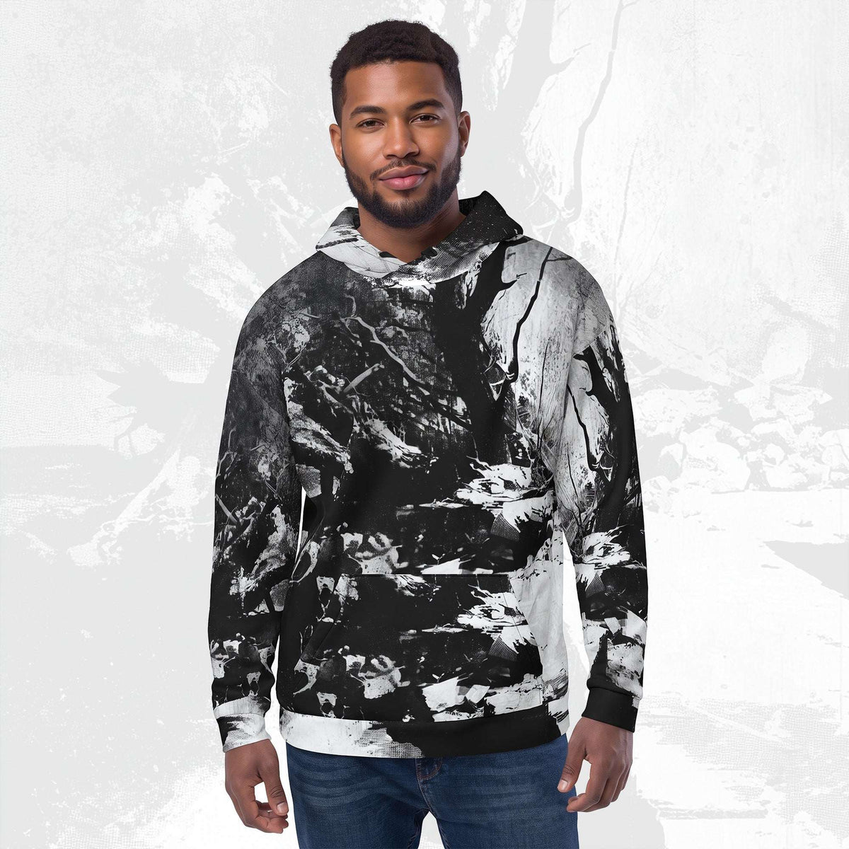 A man wearing a black and white abstract print hoodie with blue jeans, standing against a light gray textured background.