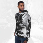 A man wearing a black and white abstract print hoodie with blue jeans, standing against a light gray textured background.