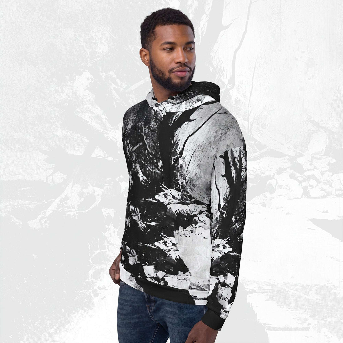 A man wearing a black and white abstract print hoodie with blue jeans, standing against a light gray textured background.