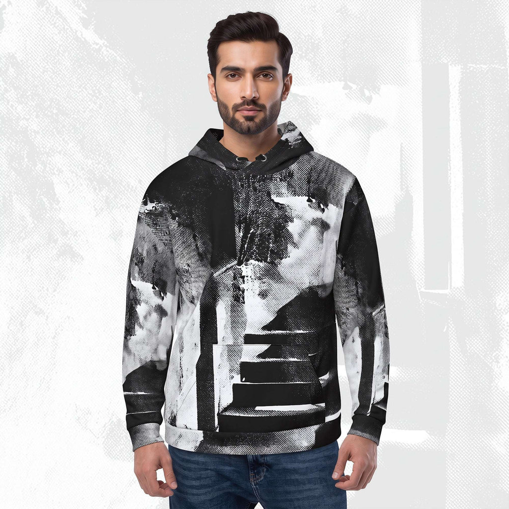 A man wearing a black and white abstract art print hoodie with a zipper, drawstrings, and kangaroo pocket, paired with blue jeans, set against a textured light gray background.