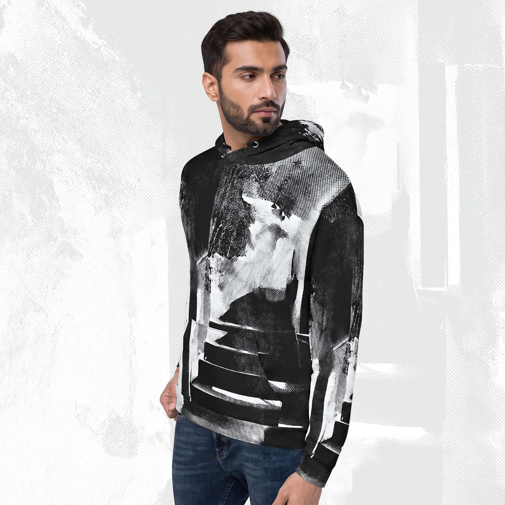 A man wearing a black and white abstract art print hoodie with blue jeans, standing against a textured white background.