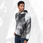 A man wearing a black, white, and gray abstract patterned hoodie with dark blue jeans, standing against a light gray textured background.