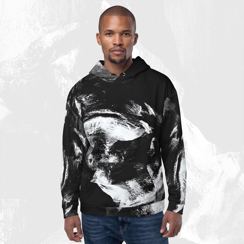 A man wearing a black pullover hoodie with a large white and gray abstract brushstroke print, paired with blue jeans, set against a light gray textured background.