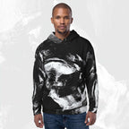 A man wearing a black pullover hoodie with a large white and gray abstract brushstroke print, paired with blue jeans, set against a light gray textured background.