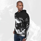 A man wearing a black pullover hoodie with a bold white abstract brushstroke pattern, paired with blue jeans, set against a light gray textured background.