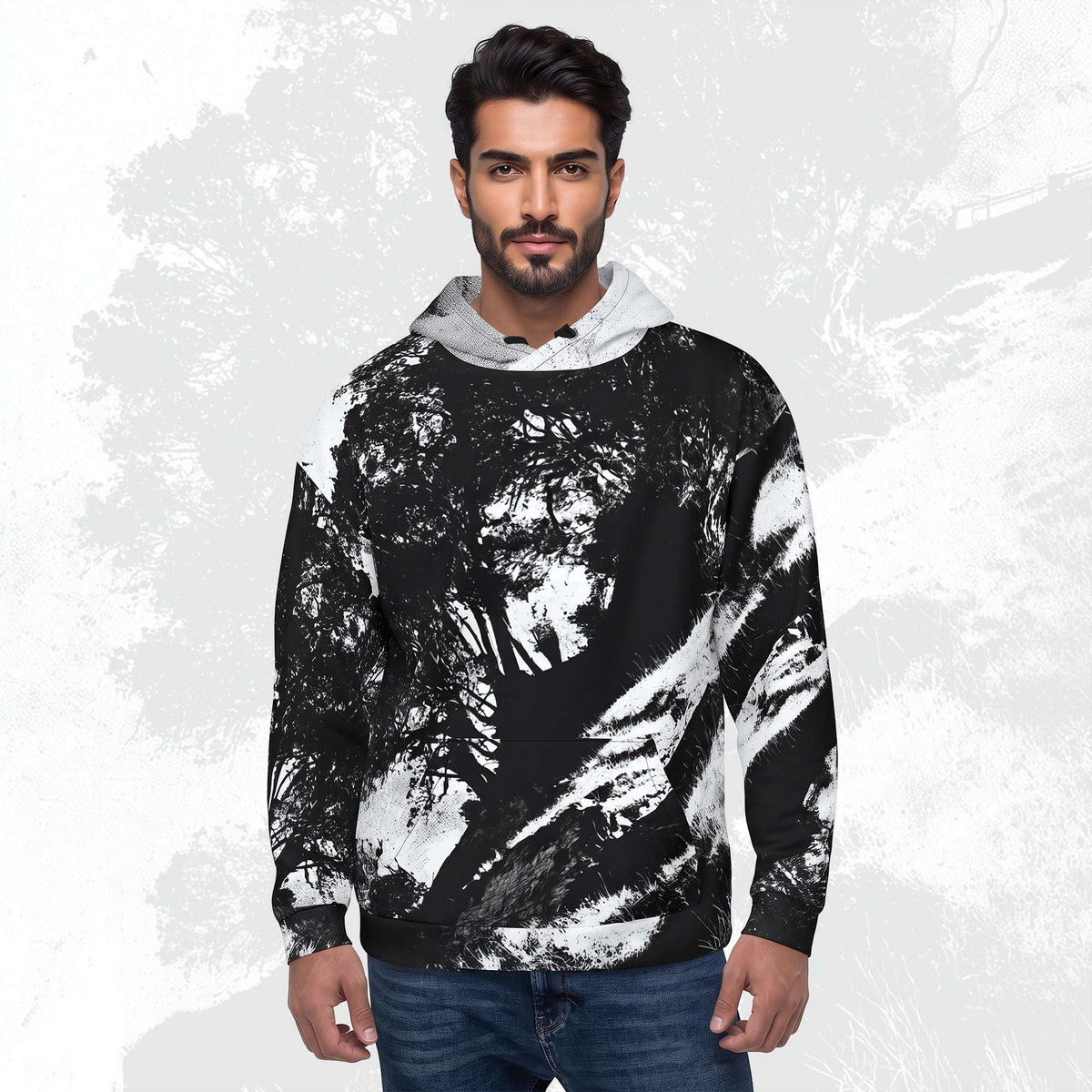 A man wearing a black and white hooded sweatshirt with an abstract brushstroke pattern, paired with blue jeans, standing against a textured light gray background.