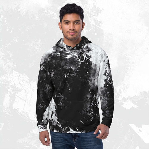 A man wearing a black and white marbled hoodie with blue jeans, standing against a textured light gray background.