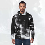 A man wearing a black and white abstract patterned hoodie with blue jeans, standing against a light gray textured background.