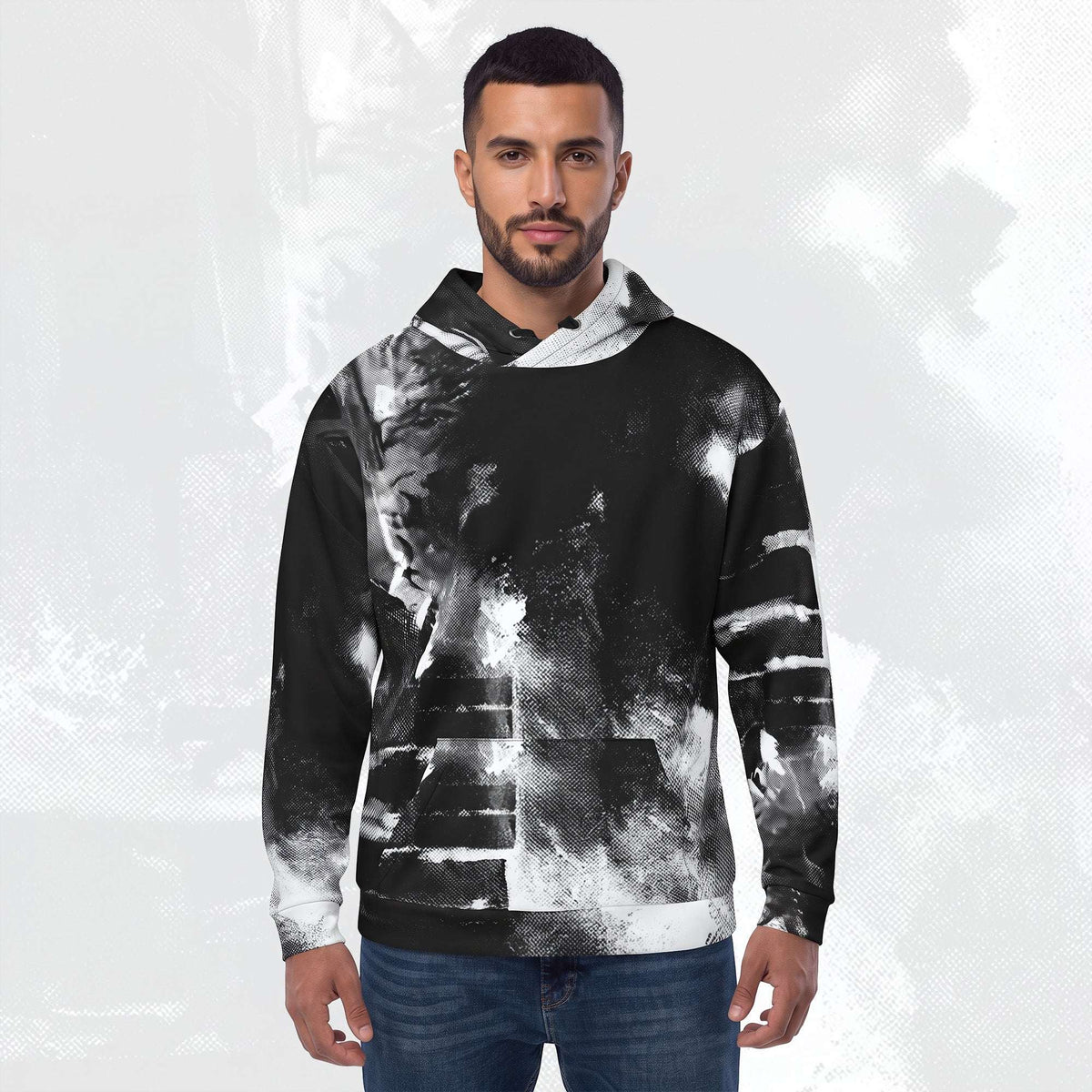 A man wearing a black and white abstract patterned hoodie with blue jeans, standing against a light gray textured background.
