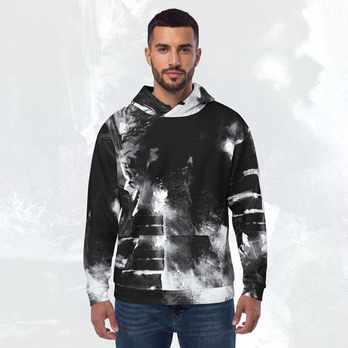 A man wearing a black and white abstract patterned hoodie with blue jeans, standing against a light gray textured background.