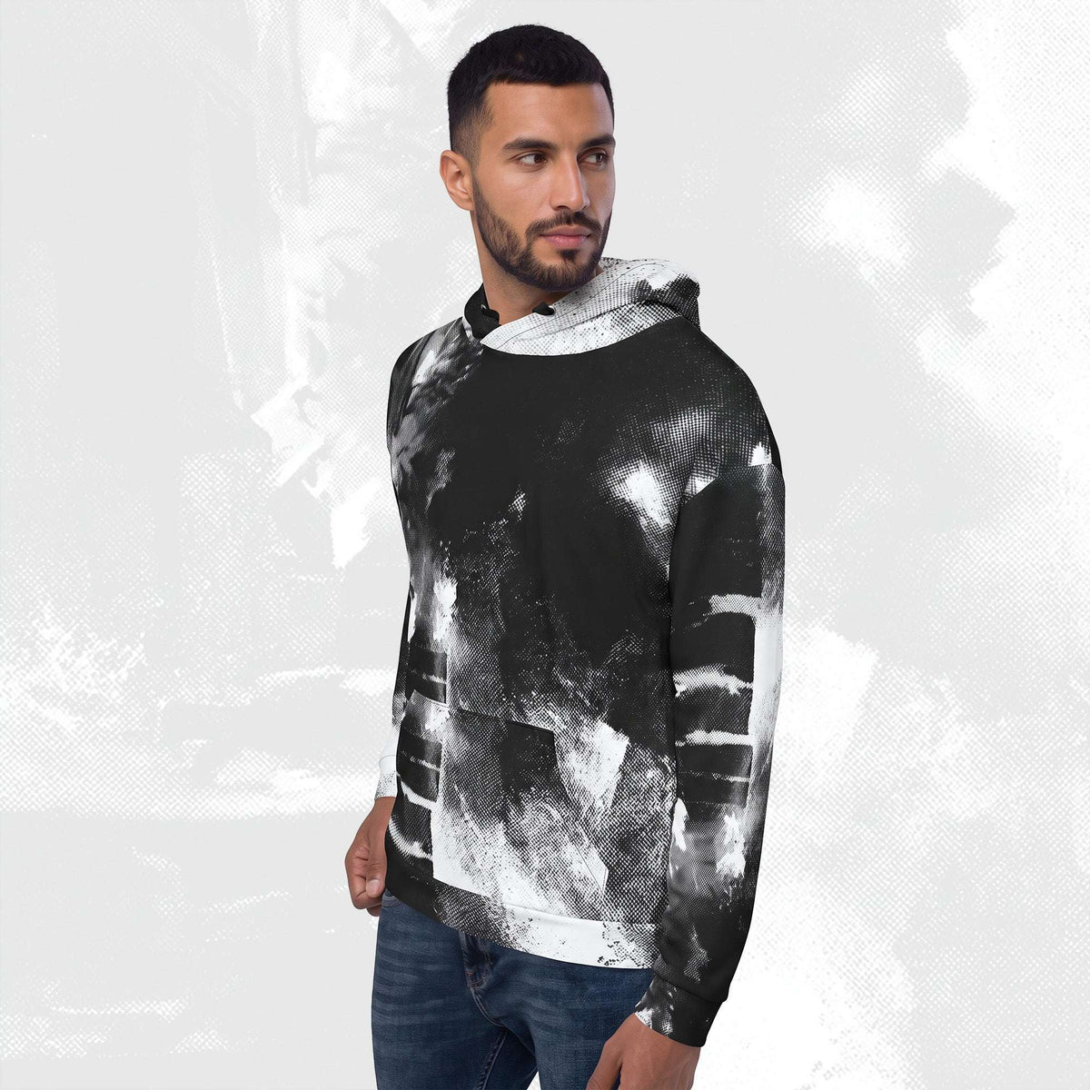 A man wearing a black and white abstract print hoodie with blue jeans, standing against a light gray textured background.