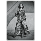 A black and white fashion photograph print featuring a woman wearing a long, flowing patterned coat and tall boots, posed against a textured architectural background.