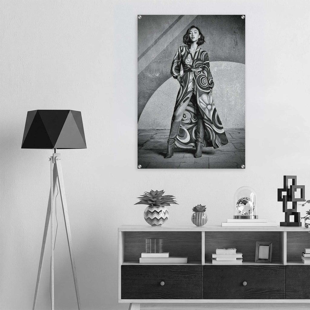 A black and white art print of a woman in a patterned robe hanging on a light gray wall above a modern shelf with decor items and a tripod floor lamp.