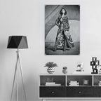 A black and white art print of a woman in a patterned robe hanging on a light gray wall above a modern shelf with decor items and a tripod floor lamp.