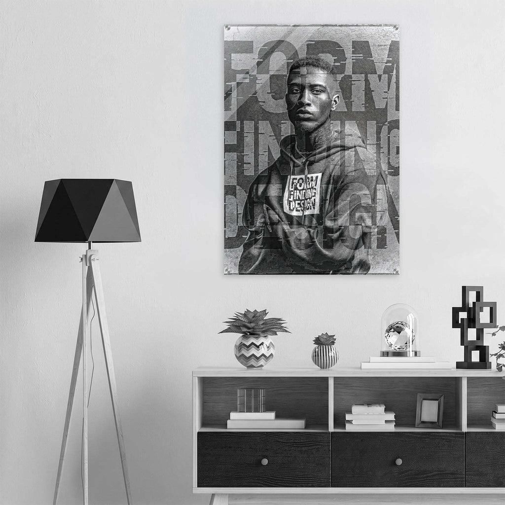 A black and white poster print of a young man wearing a hoodie with the text 'FORM FINDING DESIGN' displayed on a wall above a modern white and dark wood console shelf, next to a black tripod floor lamp.