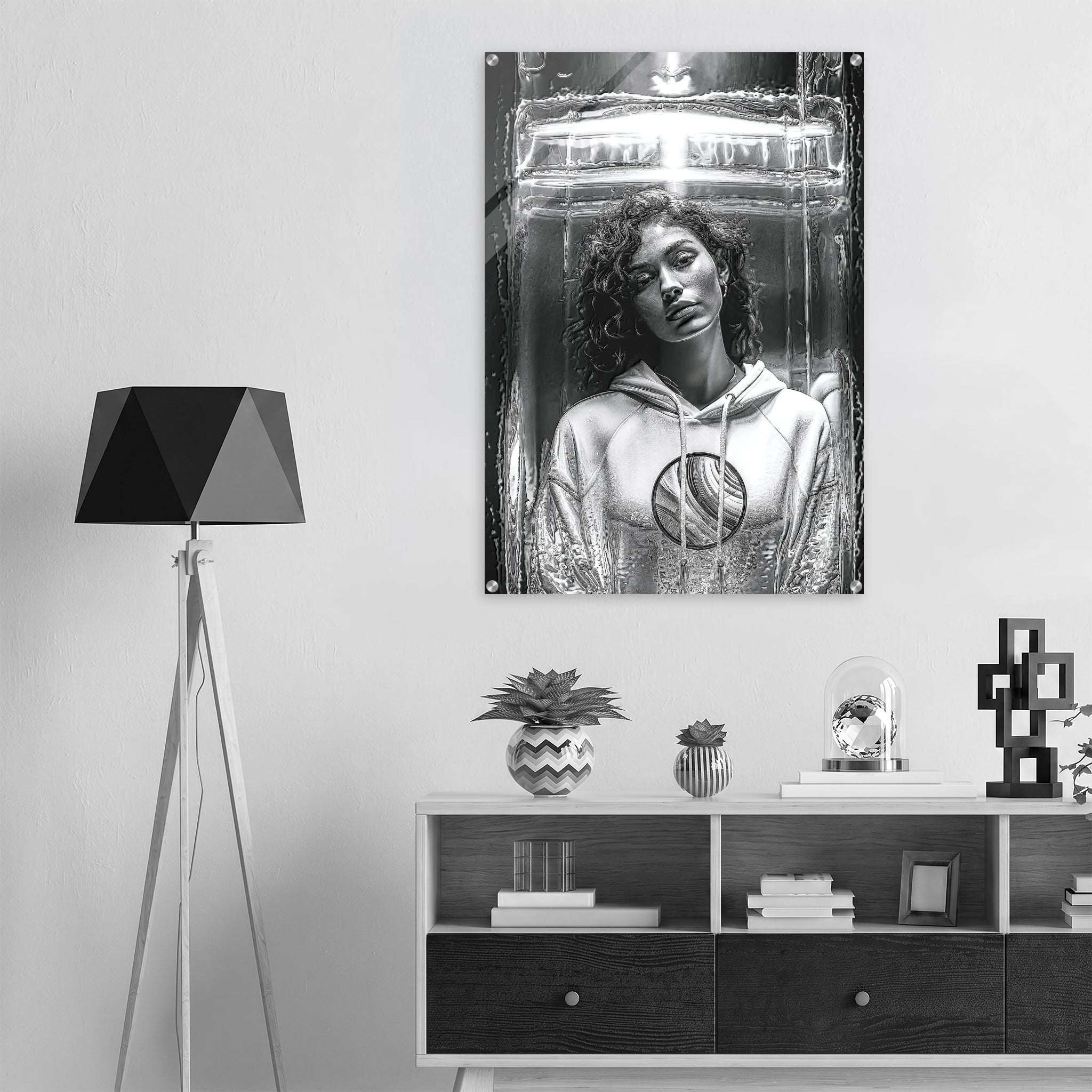A black and white poster print of a woman in a futuristic helmet hanging on a light gray wall above a dark wood console table, styled in a modern room setting with a tripod floor lamp.