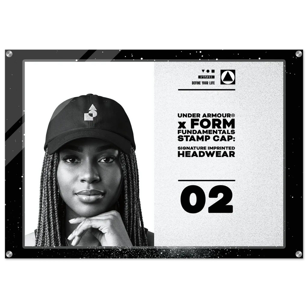 A framed black-and-white promotional print featuring a woman wearing a black Under Armour cap, with text reading 'FORM FUNDAMENTALS STAMP CAP: SIGNATURE IMPRINTED HEADWEAR' and the number 02.