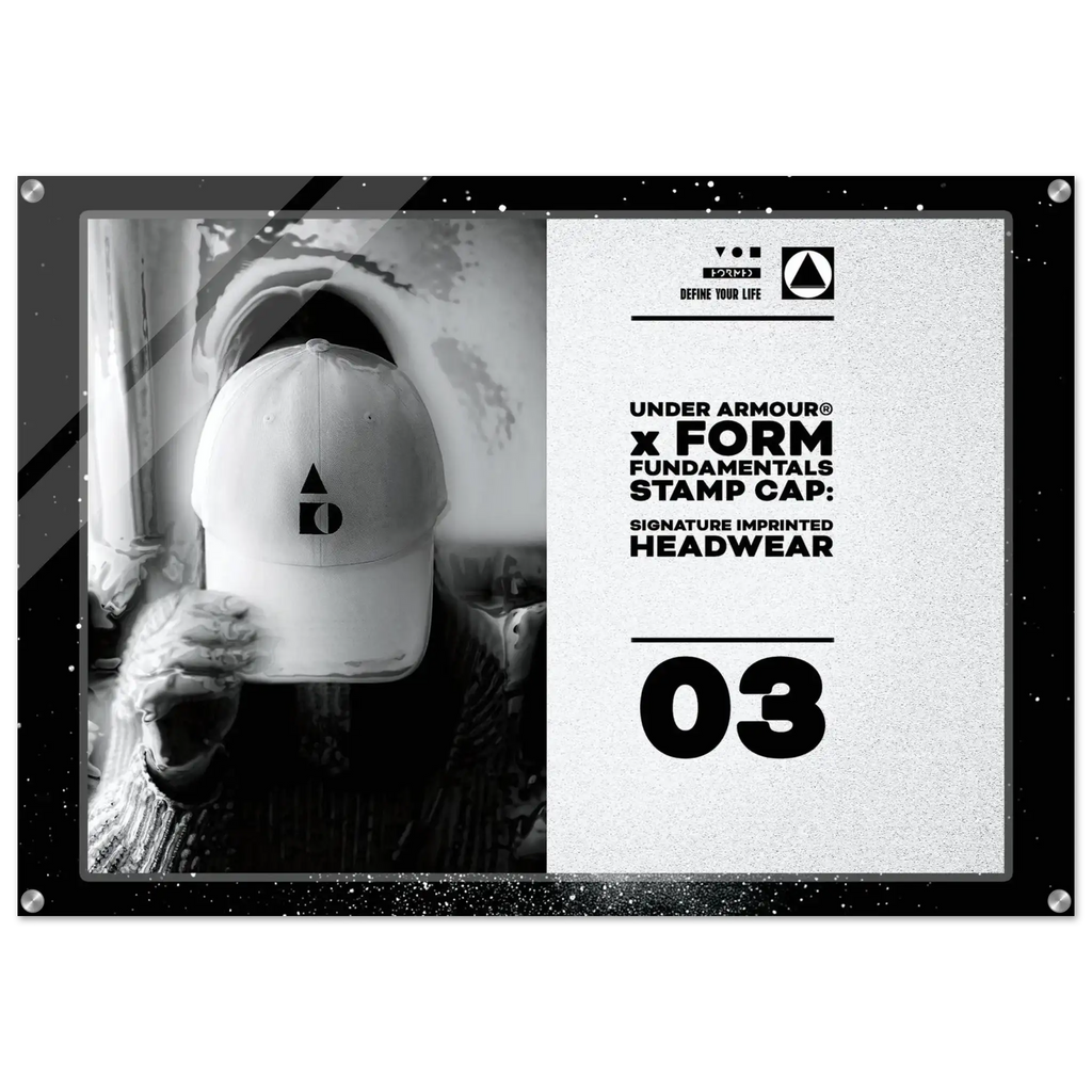 A framed monochrome promotional print or poster featuring a person in a white cap holding it in front of their face, alongside large black text reading 'UNDER ARMOUR x FORM FUNDAMENTALS STAMP CAP' and '03'. The frame has visible corner hardware and is shown against a plain white background.