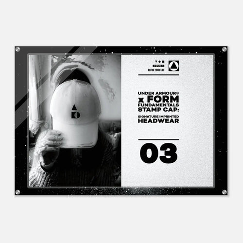 A rectangular acrylic wall art print with rounded corners and visible mounting hardware, featuring a black-and-white split design. The left side shows a monochrome photo of a person wearing a white cap, and the right side contains product text reading 'UNDER ARMOUR x FORM FUNDAMENTALS STAMP CAP' and '03'.