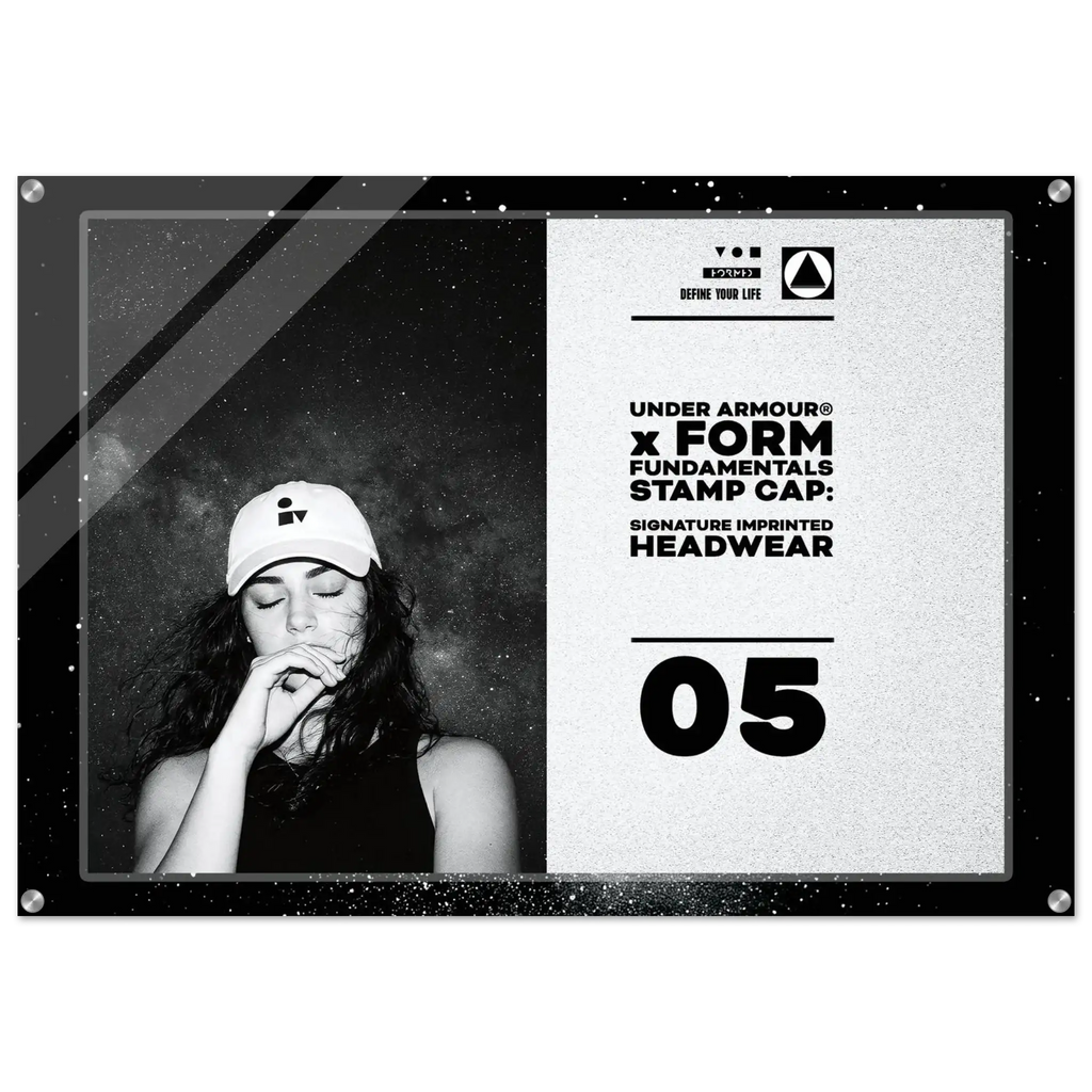 A framed monochrome promotional print or poster featuring a black-and-white portrait of a woman in a cap on the left and text on the right that reads 'UNDER ARMOUR x FORM FUNDAMENTALS STAMP CAP: SIGNATURE IMPRINTED HEADWEAR' with '05' below, shown against a light gray background.