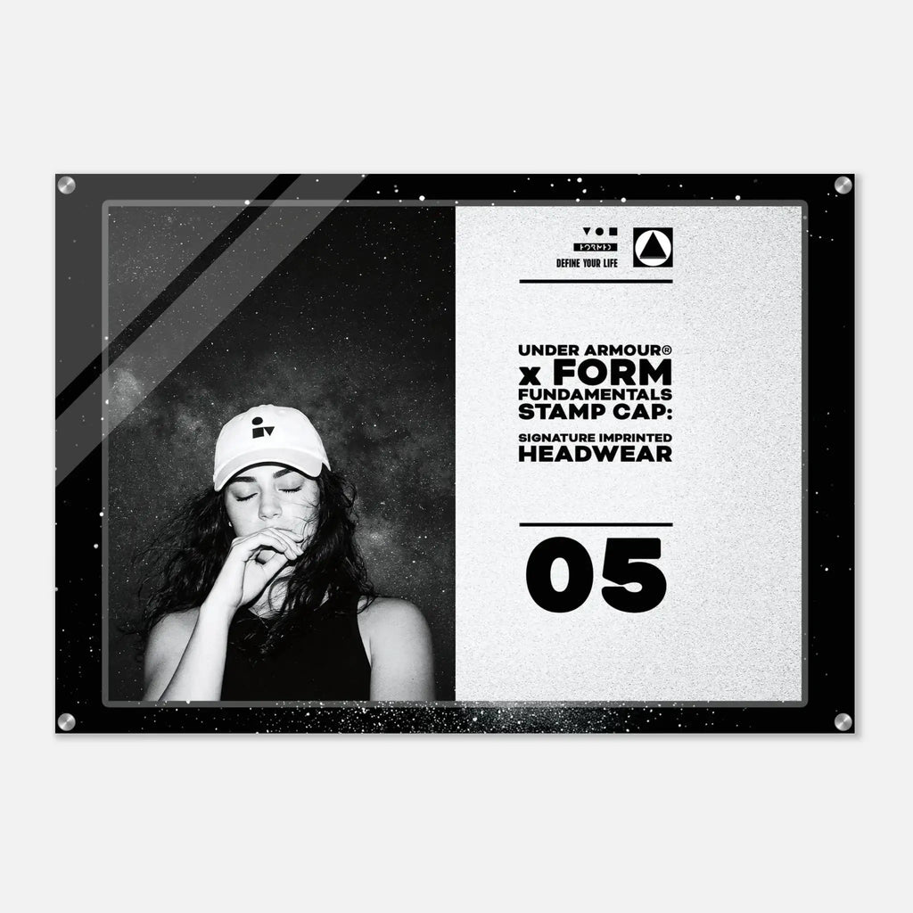 A rectangular acrylic or glass wall art print with rounded corners and visible corner hardware, shown against a light gray background. The print features a black-and-white design: the left half contains a black-and-white portrait of a woman wearing a cap, and the right half contains text reading 'UNDER ARMOUR x FORM FUNDAMENTALS STAMP CAP: SIGNATURE IMPRINTED HEADWEAR' with '05' below.