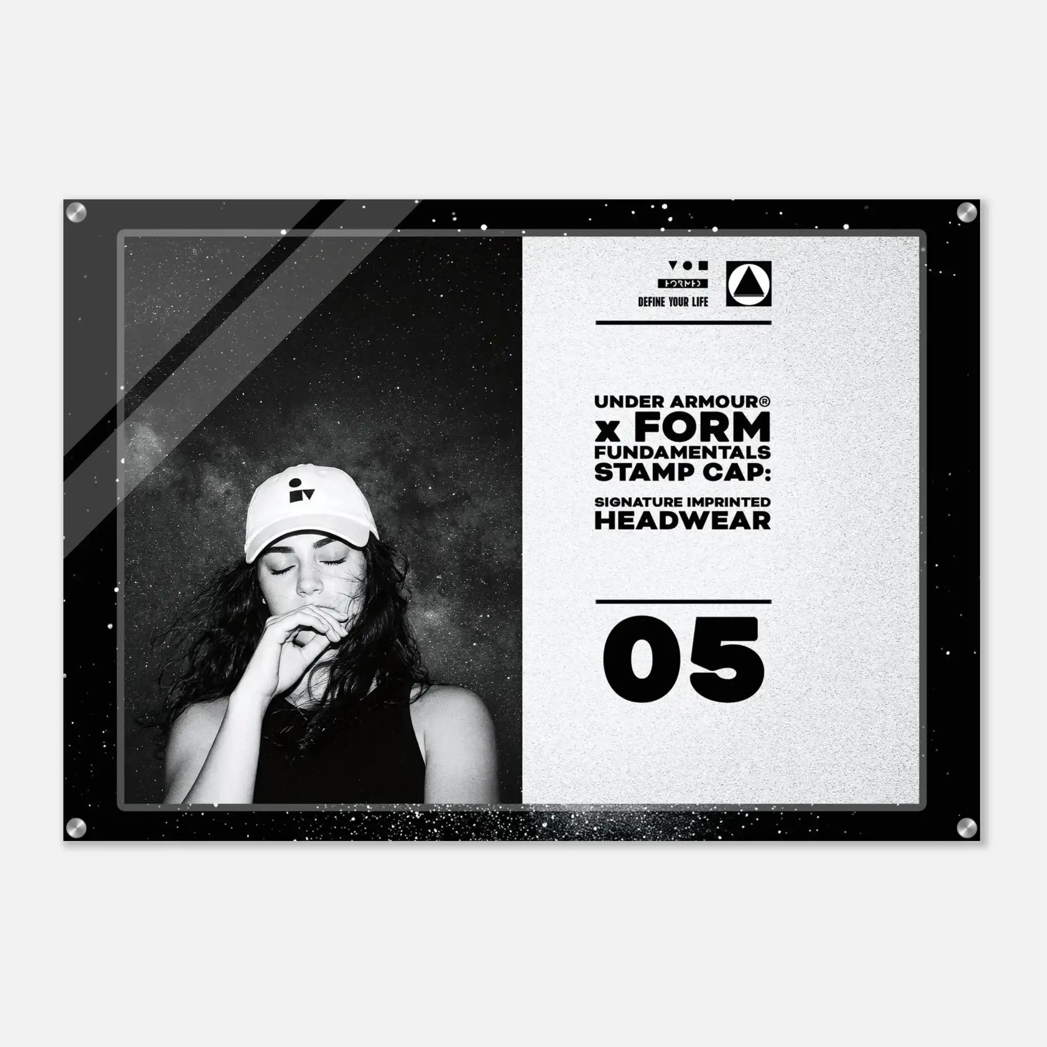A rectangular acrylic or glass wall art print with rounded corners and visible corner hardware, shown against a light gray background. The print features a black-and-white design: the left half contains a black-and-white portrait of a woman wearing a cap, and the right half contains text reading 'UNDER ARMOUR x FORM FUNDAMENTALS STAMP CAP: SIGNATURE IMPRINTED HEADWEAR' with '05' below.