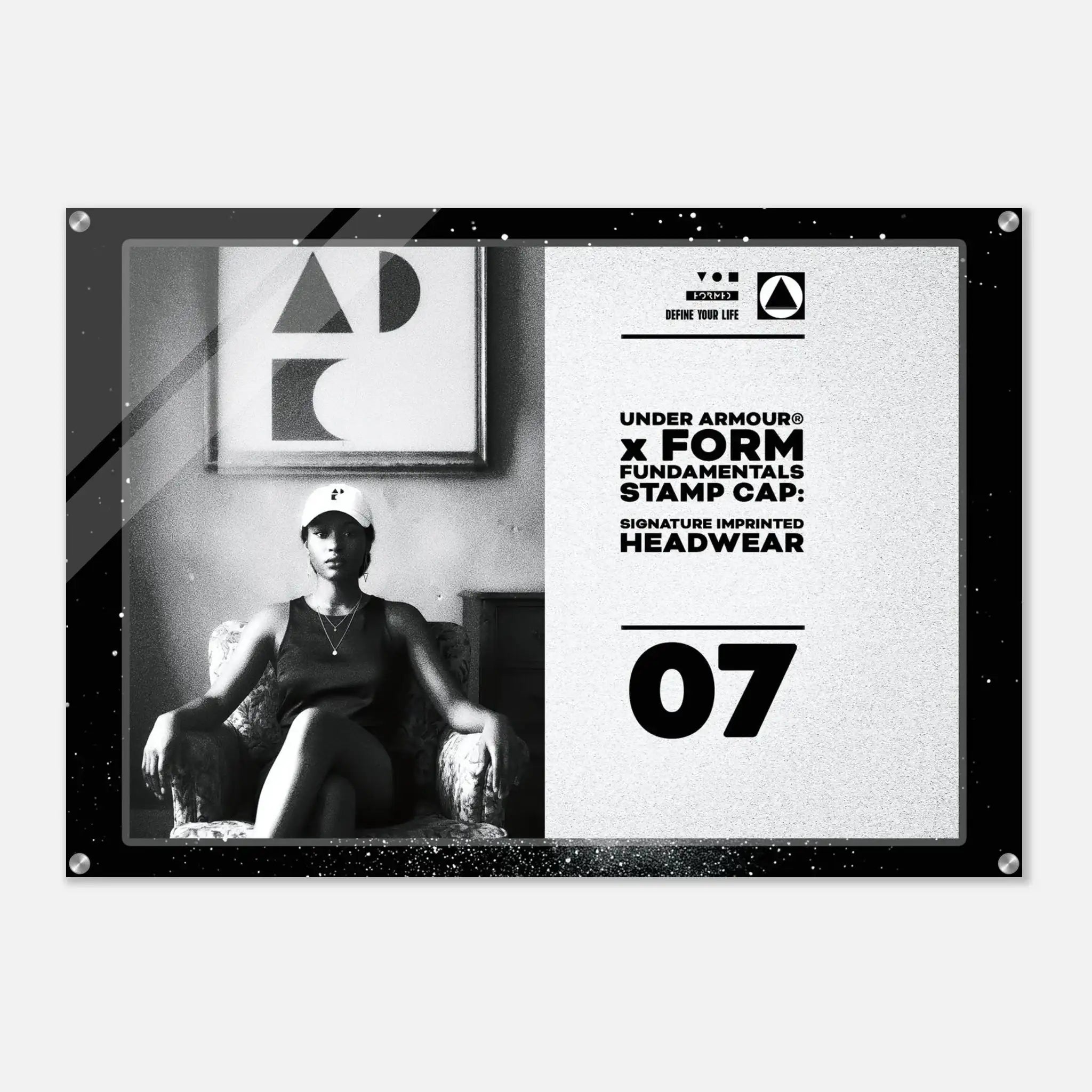 A rectangular black-framed wall art print with a split design: the left side shows a black-and-white photo of a seated woman wearing a cap, and the right side has a light textured background with Under Armour branding, text reading 'FORM FUNDAMENTALS STAMP CAP,' and the number 07.
