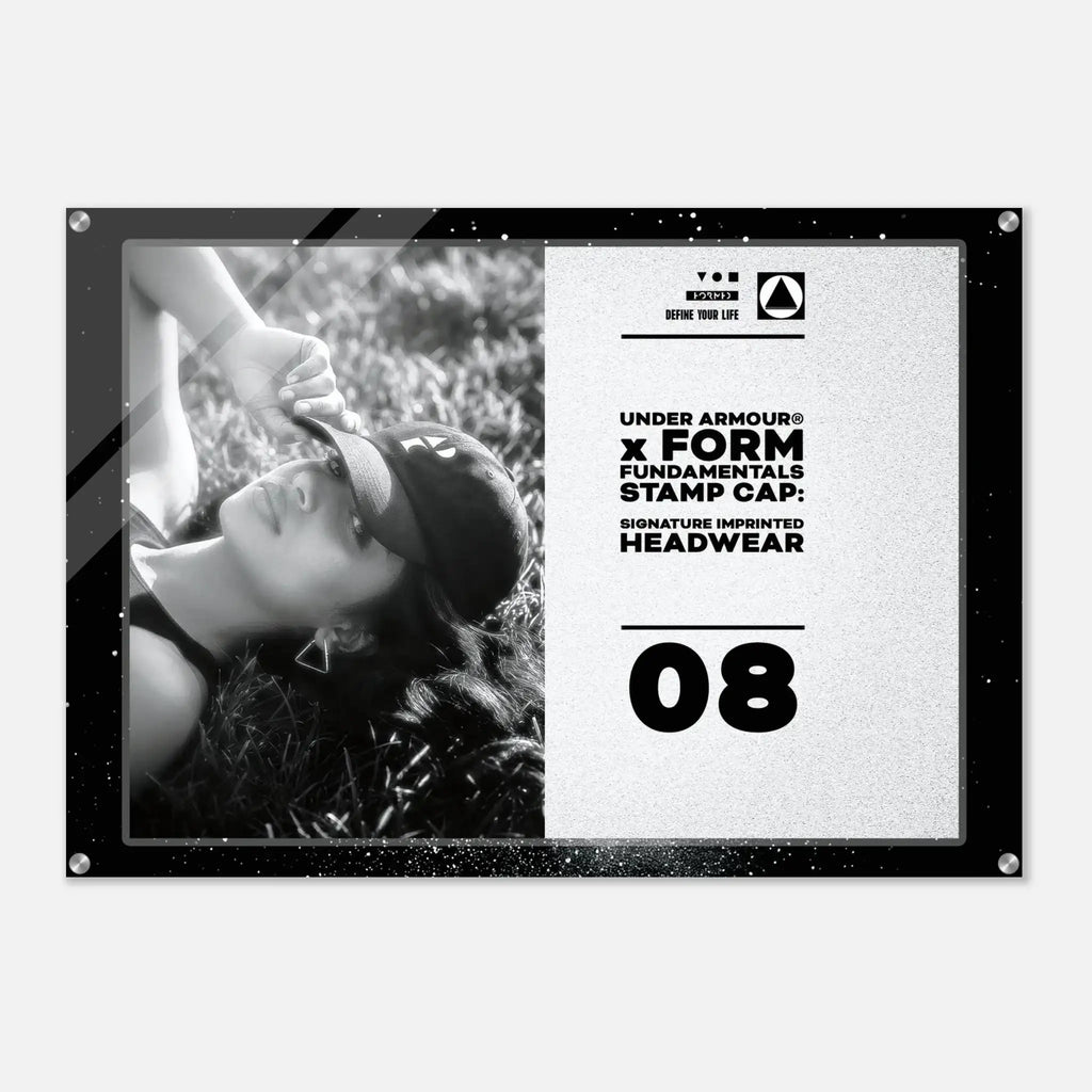 A rectangular Under Armour headwear display sign or poster with a black frame, showing a black-and-white photo of a woman wearing a cap on the left and printed text on the right including 'UNDER ARMOUR x FORM FUNDAMENTALS STAMP CAP' and the number '08'.