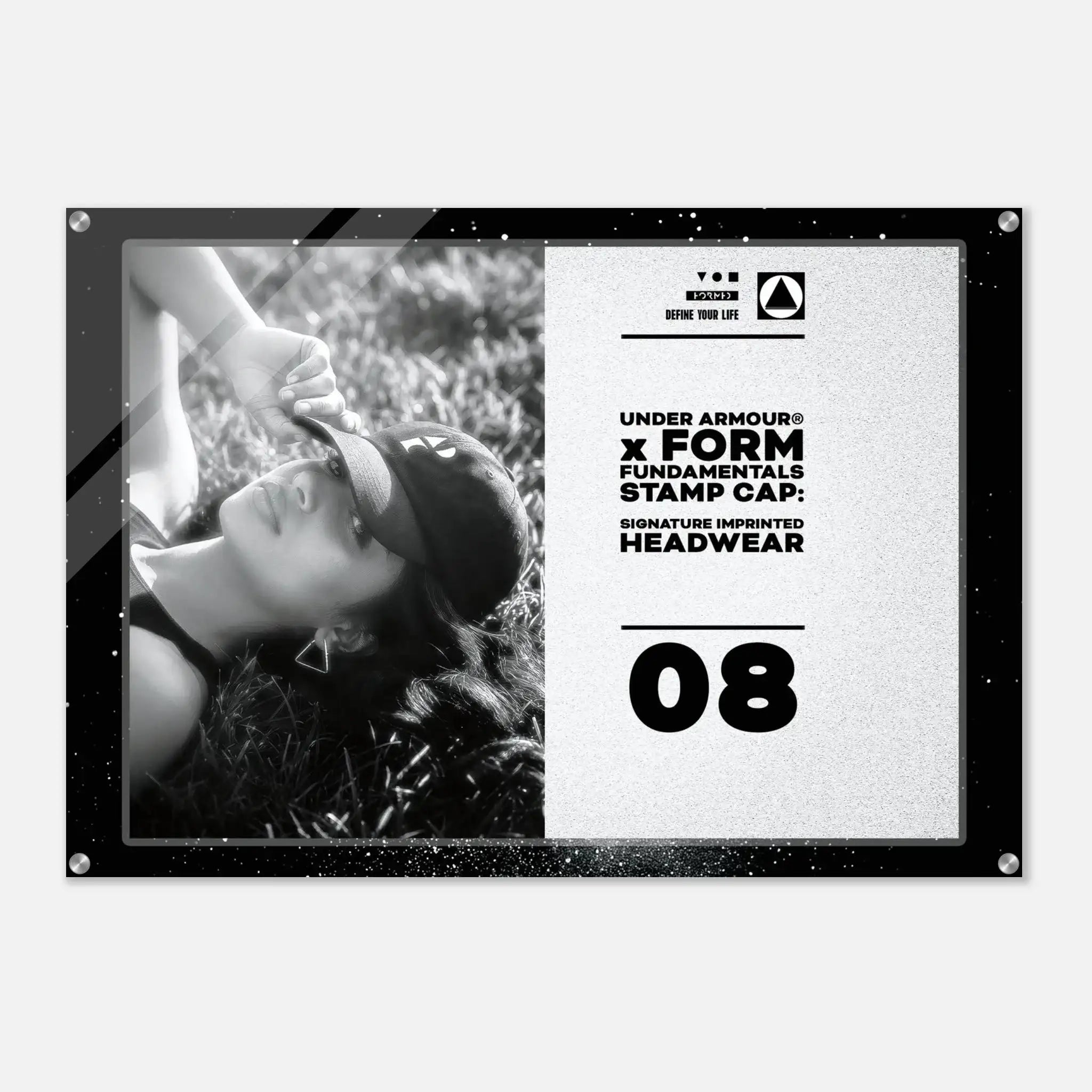 A rectangular Under Armour headwear display sign or poster with a black frame, showing a black-and-white photo of a woman wearing a cap on the left and printed text on the right including 'UNDER ARMOUR x FORM FUNDAMENTALS STAMP CAP' and the number '08'.