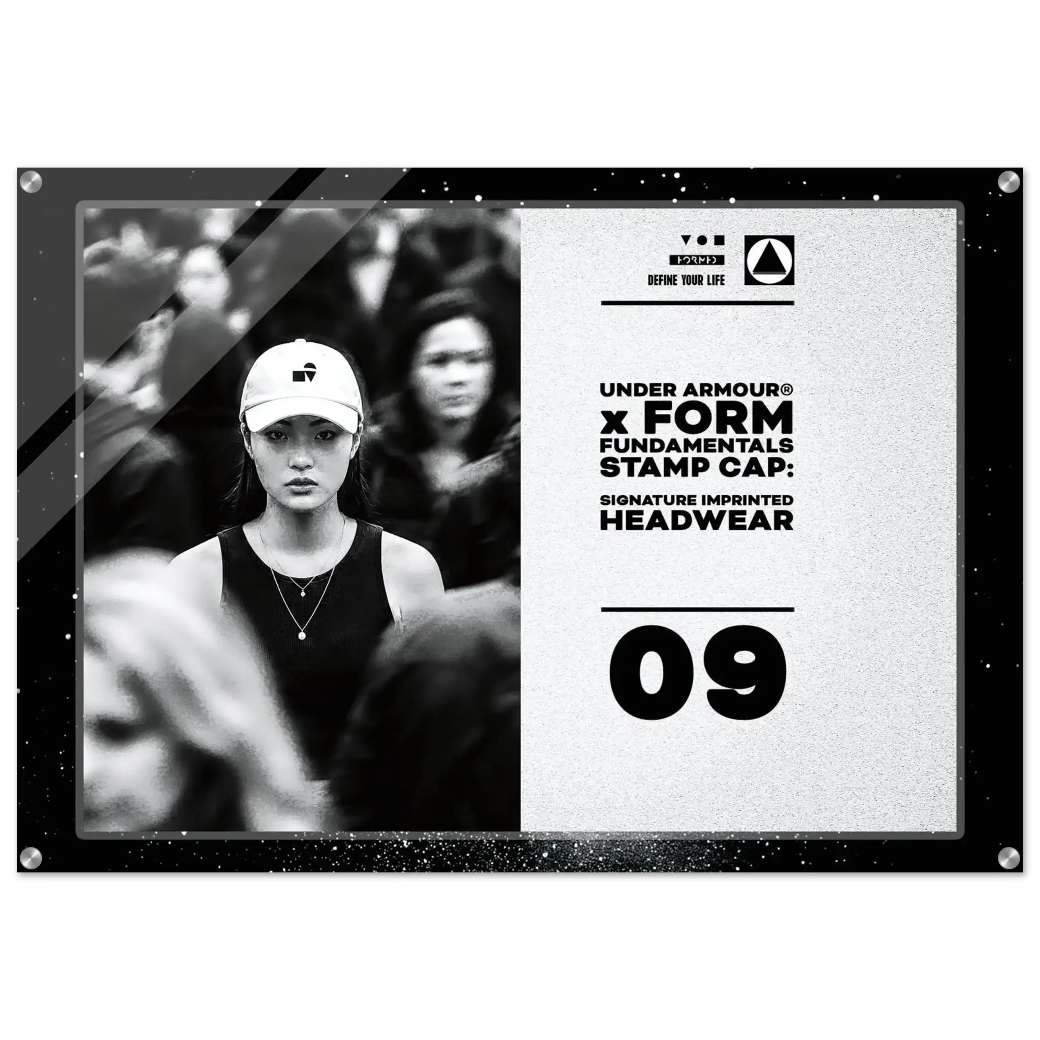 A rectangular framed print or poster with a black border, featuring a black-and-white photo of a woman in a cap on the left and printed text on the right that reads 'DEFINE YOUR LIFE UNDER ARMOUR x FORM FUNDAMENTALS STAMP CAP: SIGNATURE IMPRINTED HEADWEAR 09'.