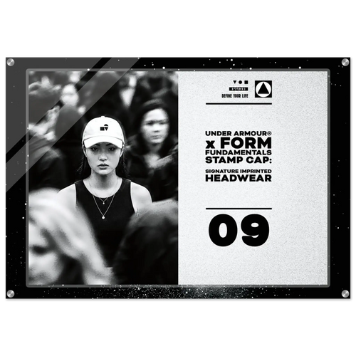 A rectangular framed print or poster with a black border, featuring a black-and-white photo of a woman in a cap on the left and printed text on the right that reads 'DEFINE YOUR LIFE UNDER ARMOUR x FORM FUNDAMENTALS STAMP CAP: SIGNATURE IMPRINTED HEADWEAR 09'.