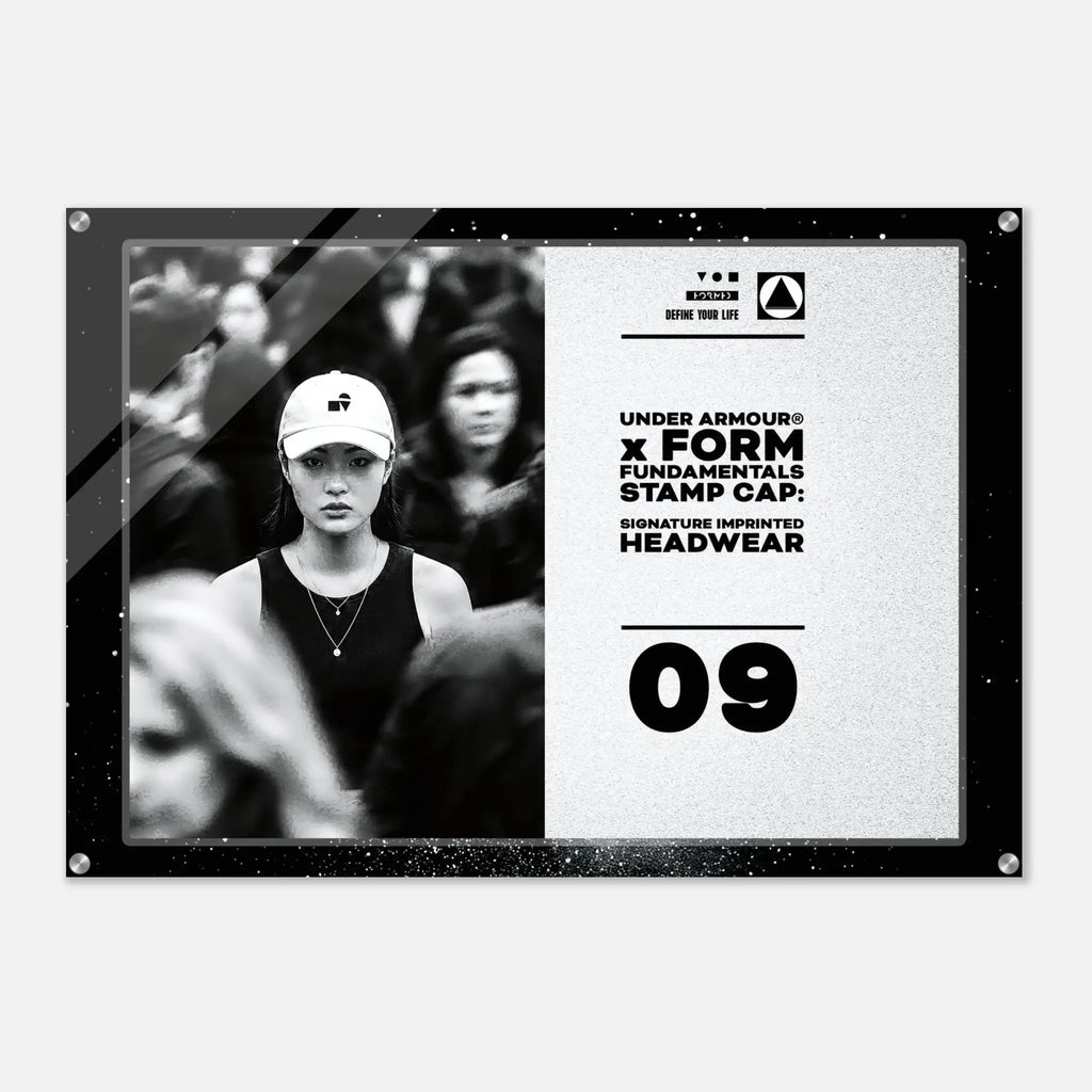 A rectangular acrylic wall art print with rounded corners and visible mounting holes, shown against a light gray background. The print features a black-and-white photo of a woman in a cap on the left and black text on a light textured right side reading 'UNDER ARMOUR x FORM FUNDAMENTALS STAMP CAP SIGNATURE IMPRINTED HEADWEAR' with '09' below.