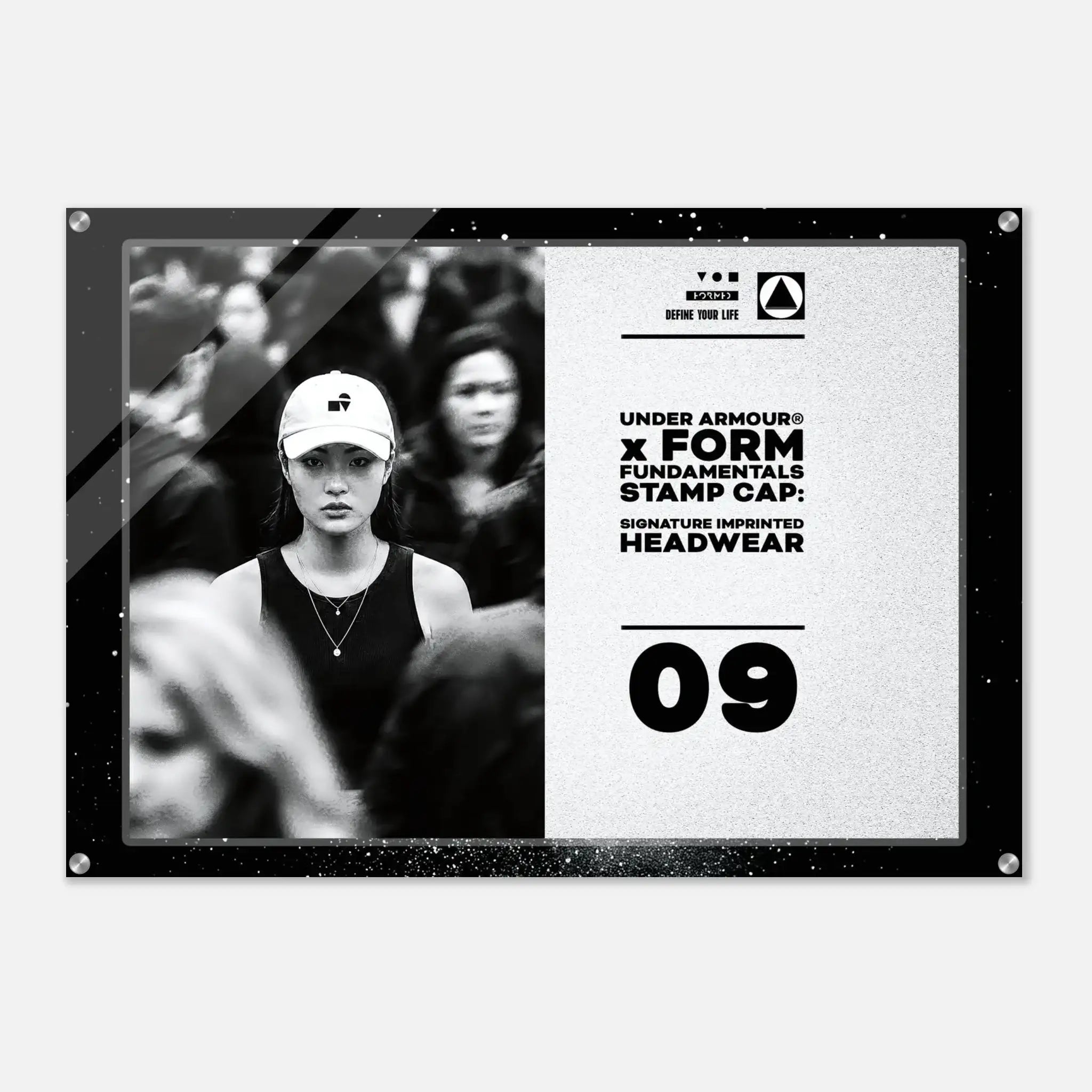 A rectangular acrylic wall art print with rounded corners and visible mounting holes, shown against a light gray background. The print features a black-and-white photo of a woman in a cap on the left and black text on a light textured right side reading 'UNDER ARMOUR x FORM FUNDAMENTALS STAMP CAP SIGNATURE IMPRINTED HEADWEAR' with '09' below.