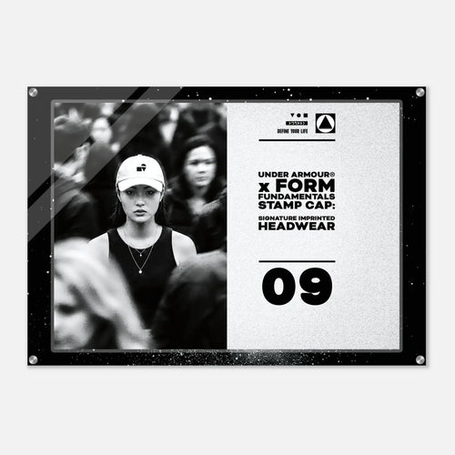 A rectangular acrylic wall art print with rounded corners and visible mounting holes, shown against a light gray background. The print features a black-and-white photo of a woman in a cap on the left and black text on a light textured right side reading 'UNDER ARMOUR x FORM FUNDAMENTALS STAMP CAP SIGNATURE IMPRINTED HEADWEAR' with '09' below.