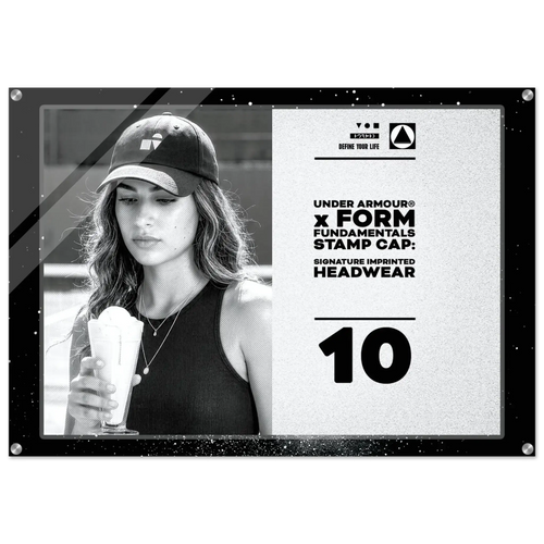 A rectangular promotional print or poster with a black border, featuring a black-and-white photo of a woman wearing an Under Armour cap and holding a drink, alongside printed text on a light background. The visible text includes 'UNDER ARMOUR x FORM FUNDAMENTALS STAMP CAP: SIGNATURE IMPRINTED HEADWEAR' and the number '10'.